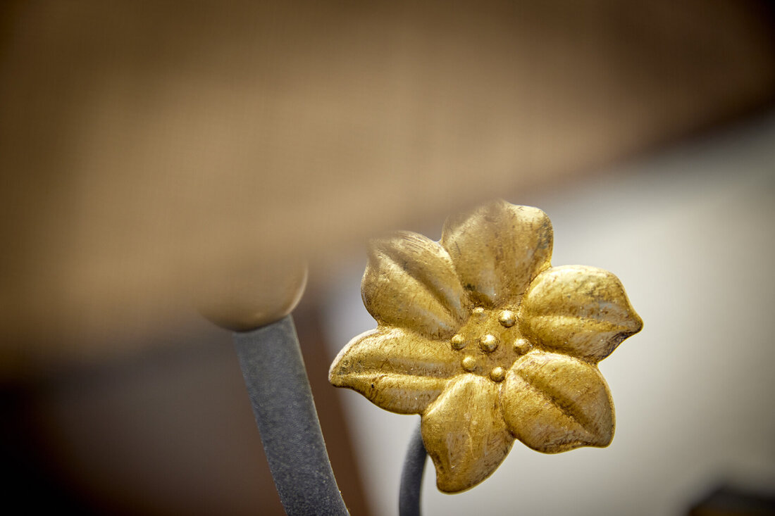 Eine goldene Blume mit detaillierten Blütenblättern und einer zentralen Struktur, die auf einem grauen Stiel sitzt.