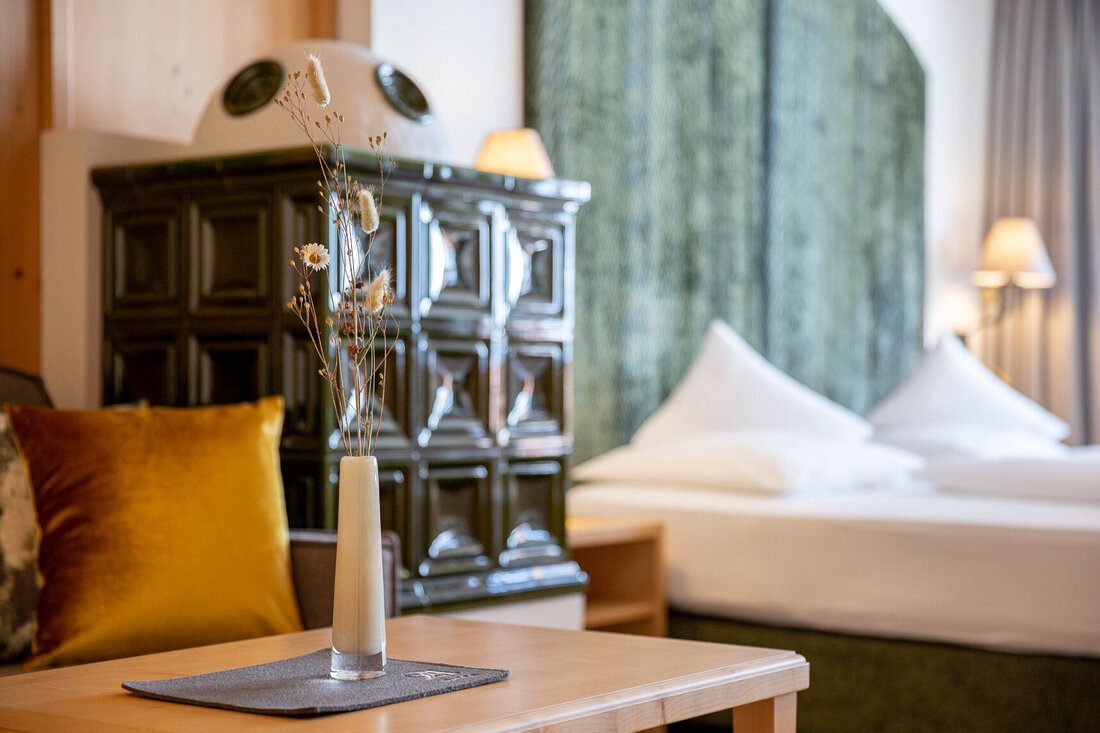 Ein eleganter Couchtisch mit einer Vase, gefüllt mit Trockenblumen, steht in einem gemütlichen Raum mit einem Bett im Hintergrund.