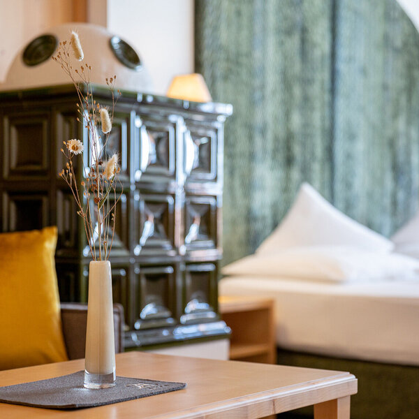 Ein eleganter Couchtisch mit einer Vase, gefüllt mit Trockenblumen, steht in einem gemütlichen Raum mit einem Bett im Hintergrund.