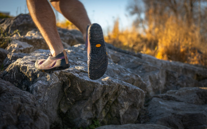 Ein Mann mit violetten Schuhen geht über Steine.
