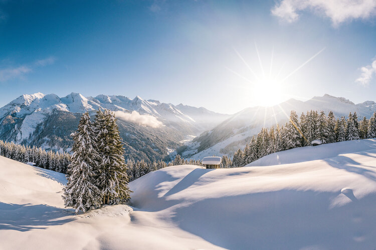 Eine atemberaubende Winterlandschaft mit schneebedeckten Bergen und strahlender Sonne, die über die Hügel scheint.