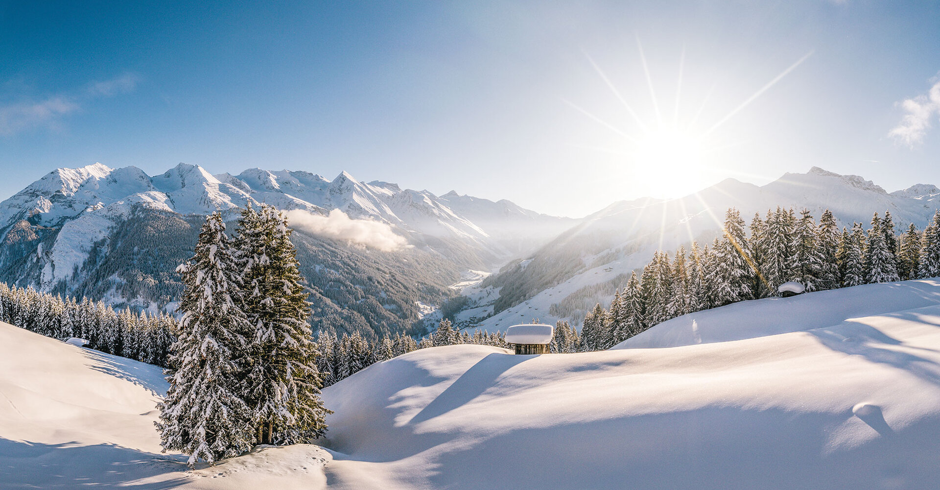 Eine atemberaubende Winterlandschaft mit schneebedeckten Bergen und strahlender Sonne, die über die Hügel scheint.