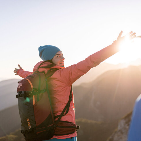 Die Wanderin in der pinken Jacke strahlt Freude aus, während sie die Sonne hinter den Bergen begrüßt.