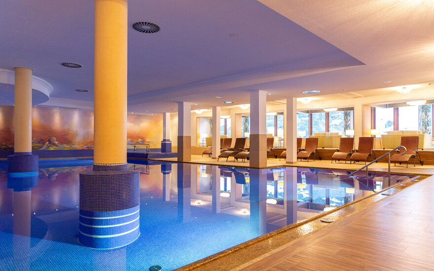 Ein eleganter Innenpool mit blauen Fliesen, umgeben von gemütlichen Liegen und sanftem Licht, das eine entspannende Atmosphäre schafft.