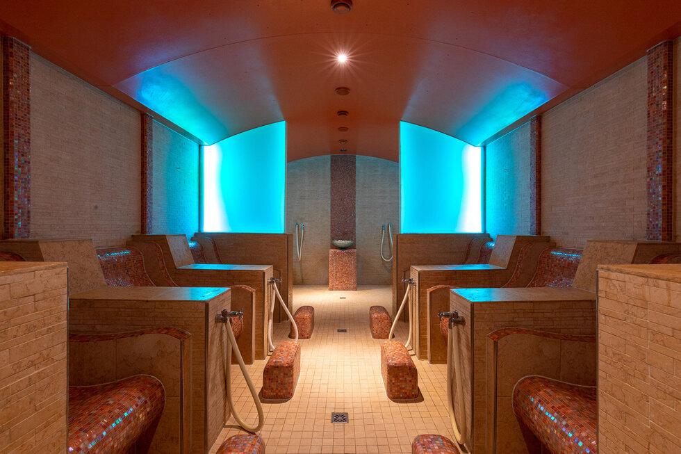 Der Innenraum einer modernen Sauna, ausgestattet mit bequemen Liegen und beruhigenden blauen Lichtakzenten für eine entspannende Atmosphäre.
