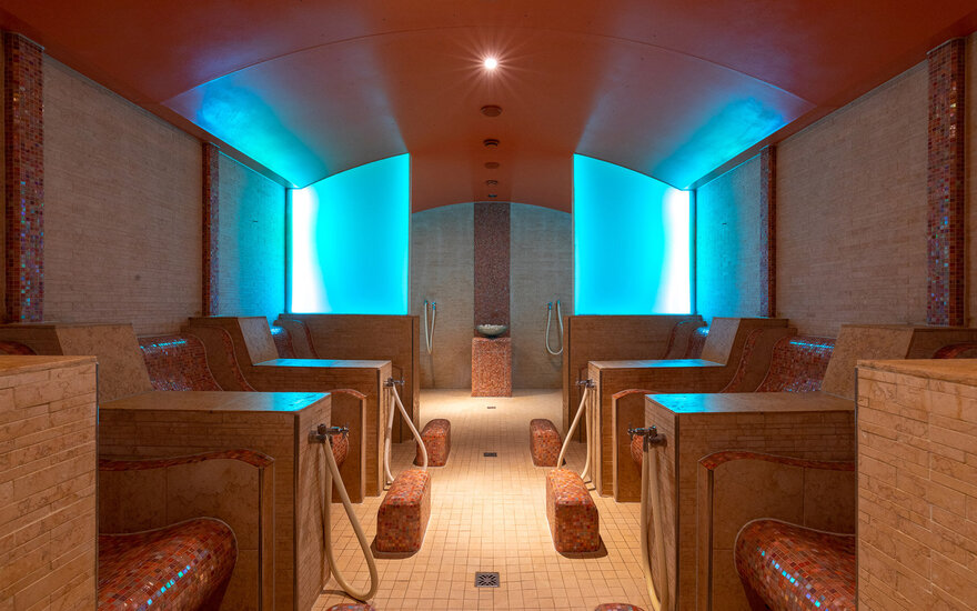 Der Innenraum einer modernen Sauna, ausgestattet mit bequemen Liegen und beruhigenden blauen Lichtakzenten für eine entspannende Atmosphäre.
