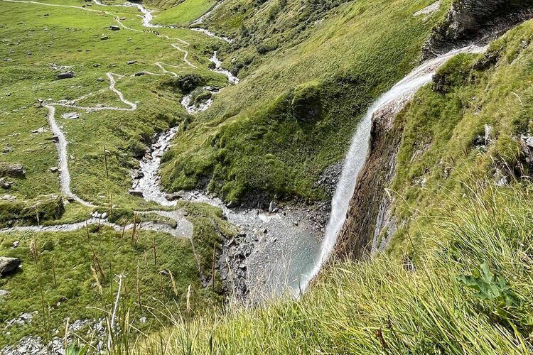 Ein Wasserfall stürzt über eine grüne Klippe, umgeben von saftigem Gras und einem klaren, plätschernden Bach.