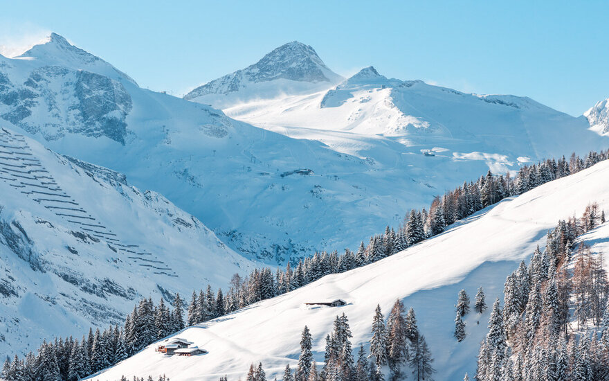 Eine atemberaubende Winterlandschaft mit schneebedeckten Bergen und einem klaren blauen Himmel, der die Szene erhellt.
