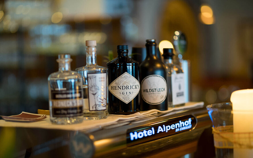 Der Tresen des Hotel Alpenhof zeigt eine Auswahl an Spirituosen, darunter Hendrick's Gin und eine brennende Kerze.