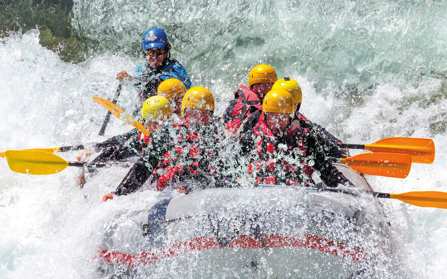 Eine Gruppe von Rafting-Abenteurern paddelt energisch durch schäumende Wellen, während Wasser spritzt und sprudelt.