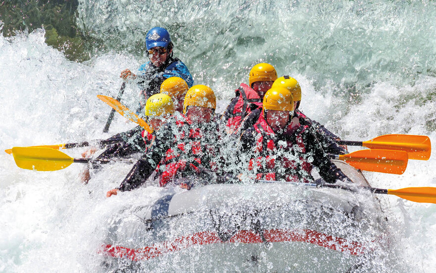 Eine Gruppe von Rafting-Abenteurern paddelt energisch durch schäumende Wellen, während Wasser spritzt und sprudelt.