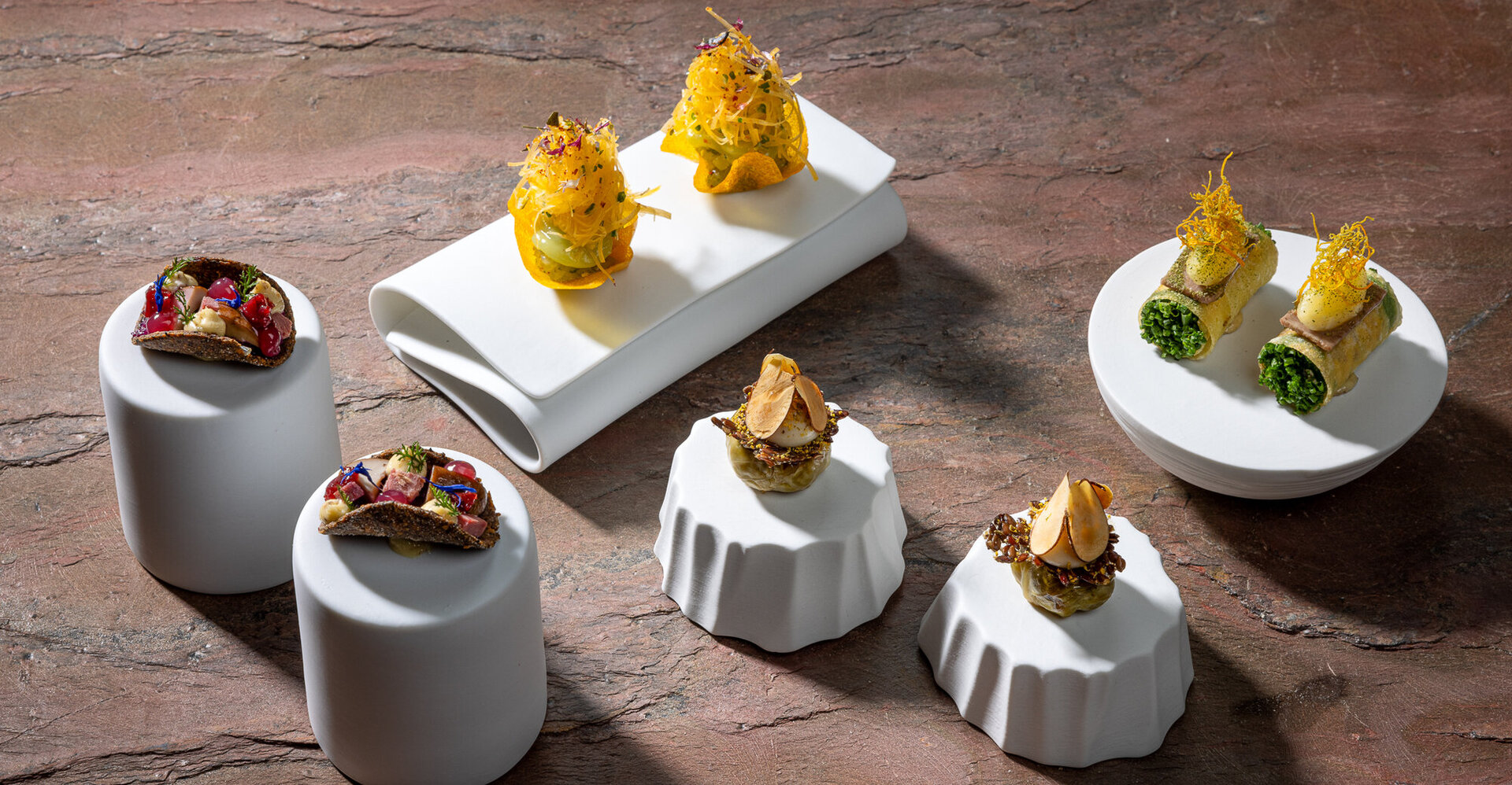 Elegante Häppchen mit verschiedenen Zutaten, kunstvoll auf weißen Tellern angerichtet, die eine moderne kulinarische Präsentation zeigen.