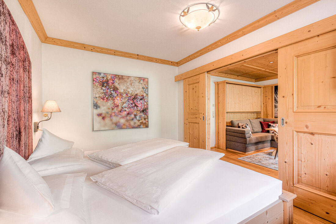 Ein gemütliches Schlafzimmer mit einem großen Bett, einem modernen Kunstwerk und warmen Holzelementen im Hintergrund.