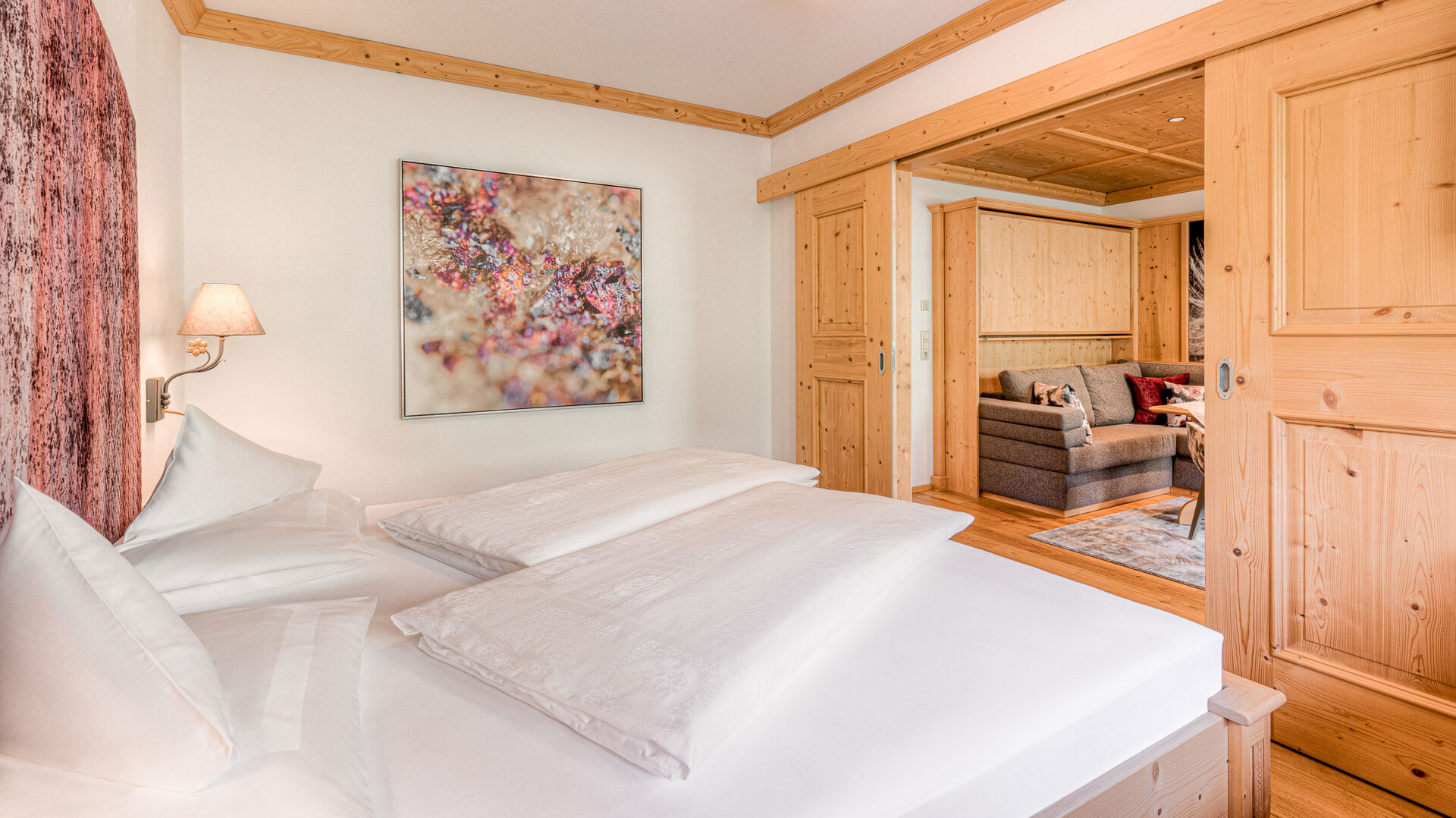 Ein gemütliches Schlafzimmer mit einem großen Bett, einem modernen Kunstwerk und warmen Holzelementen im Hintergrund.