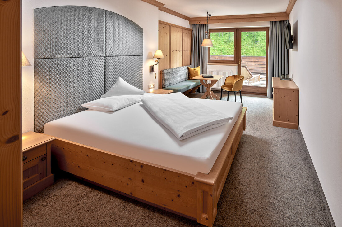 Ein gemütliches Schlafzimmer mit einem großen Bett, einem gepolsterten Kopfteil und warmen Holzmöbeln, die eine einladende Atmosphäre schaffen.