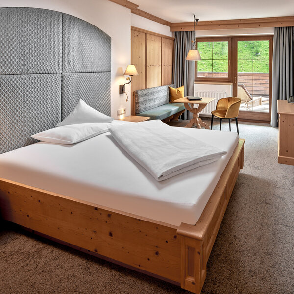 Ein gemütliches Schlafzimmer mit einem großen Bett, einem gepolsterten Kopfteil und warmen Holzmöbeln, die eine einladende Atmosphäre schaffen.