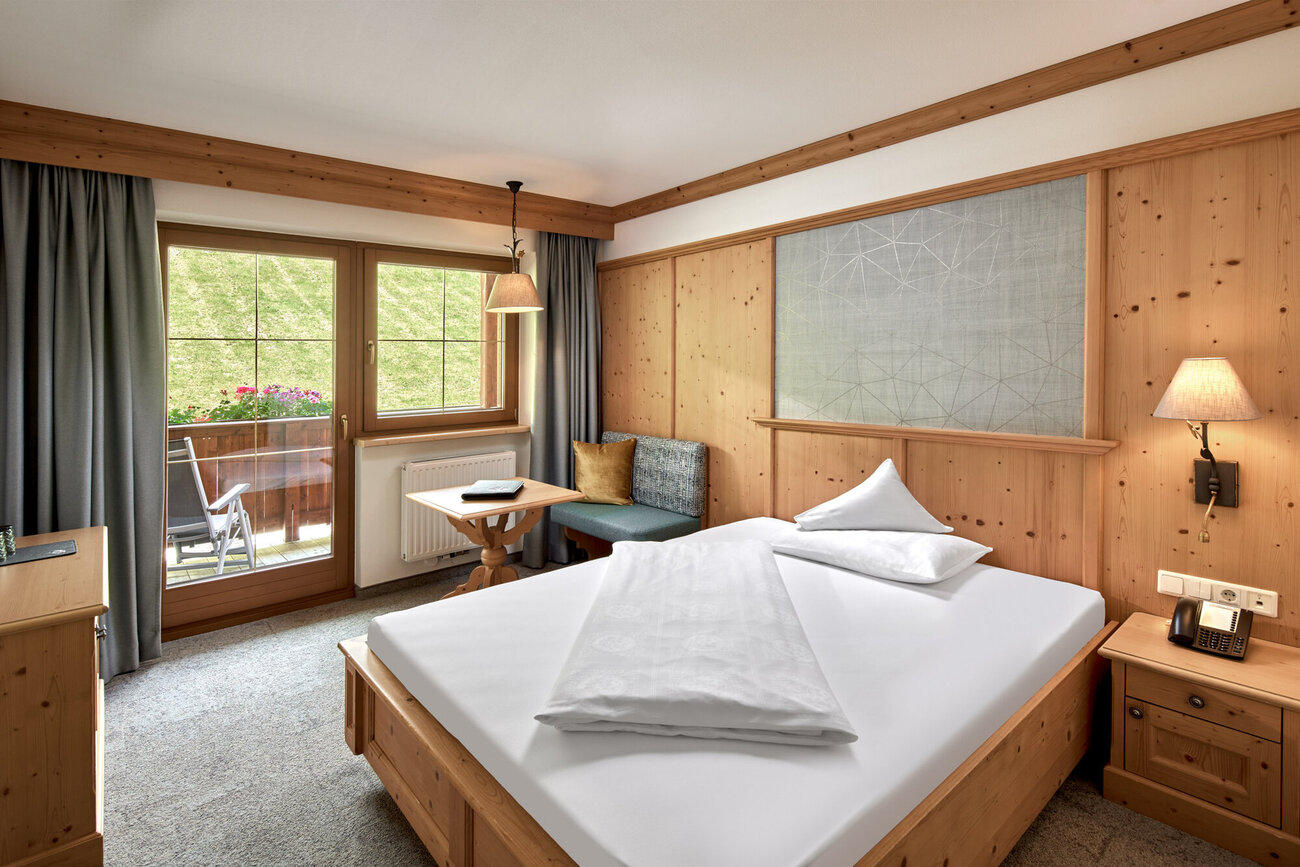 Ein gemütliches Zimmer mit einem großen Bett, Holzverkleidung und einem Fenster, das auf eine grüne Wiese blickt.