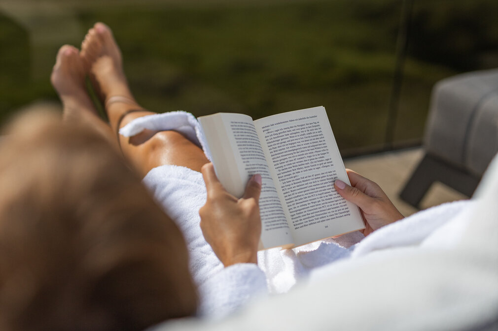 Eine Person ließt ein Buch auf einer Liege.