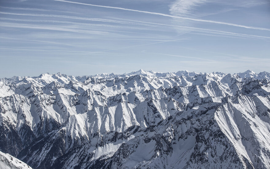 Eine beeindruckende Berglandschaft mit schneebedeckten Gipfeln unter einem klaren blauen Himmel und feinen Wolkenstreifen.