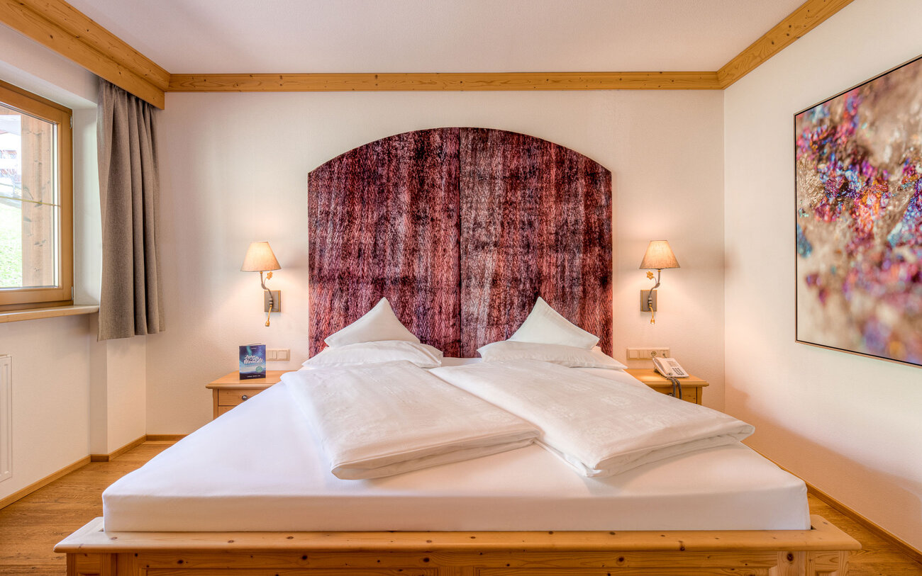 Ein gemütliches Schlafzimmer mit einem großen Doppelbett, das von einer eleganten, gemusterten Wandverkleidung umgeben ist.