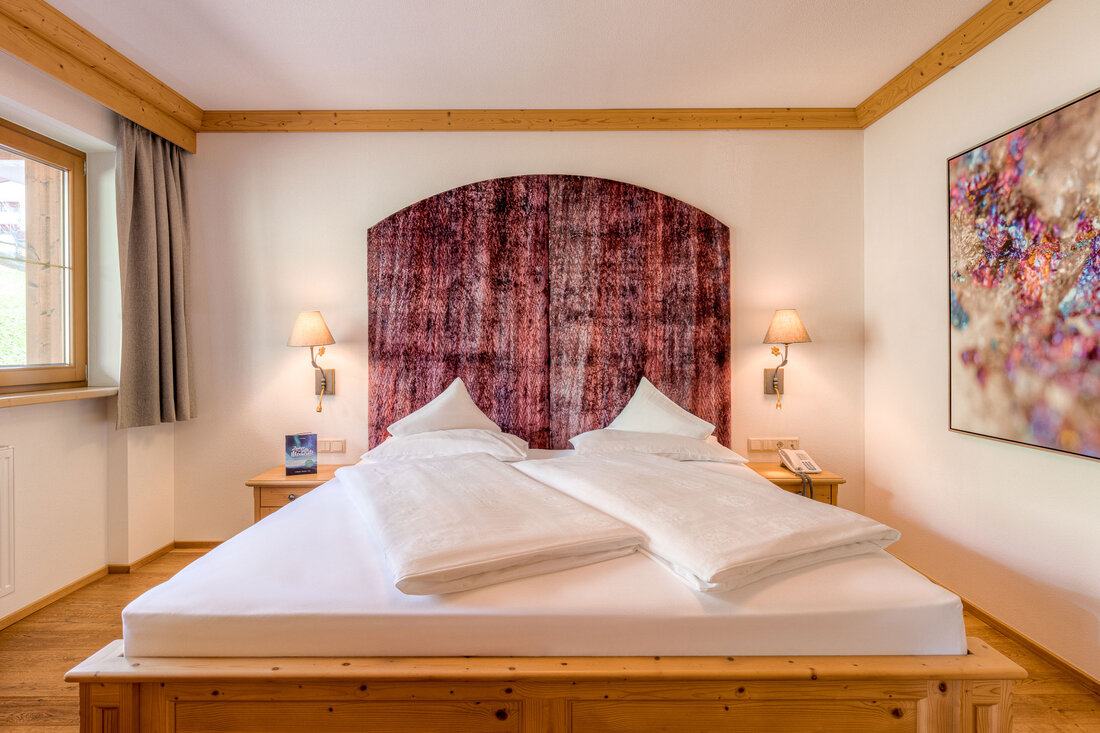 Ein gemütliches Schlafzimmer mit einem großen Doppelbett, das von einer eleganten, gemusterten Wandverkleidung umgeben ist.