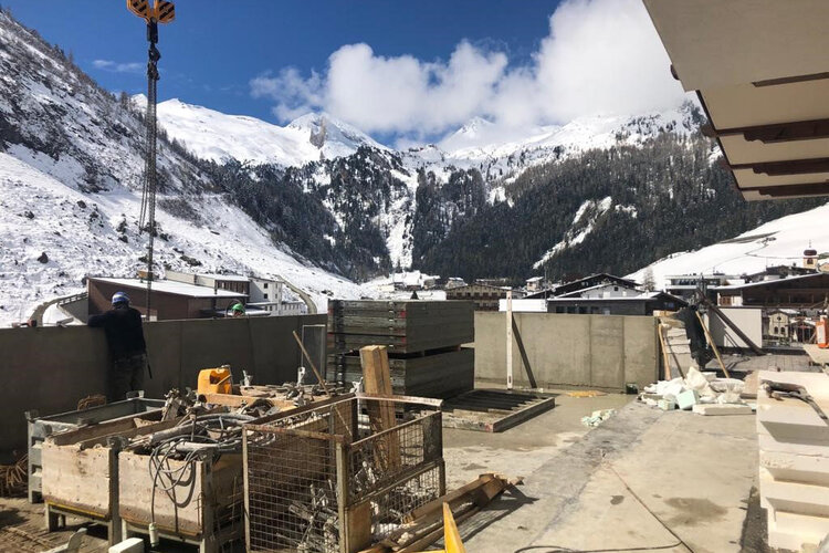 Eine Baustelle mit einem Blick auf schneebedeckte Berge und Wolken, während Arbeiter an der Wand arbeiten.