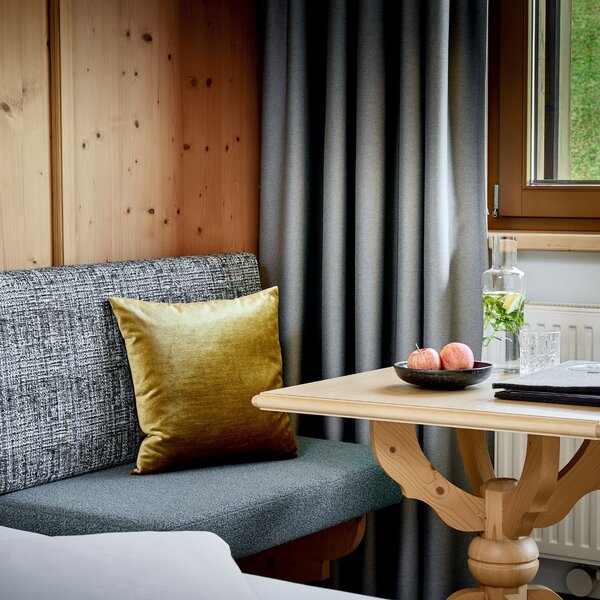 Ein gemütlicher Sitzbereich mit einem grauen Sofa und einem goldenen Kissen, umgeben von Holzpaneelen und Vorhängen.