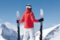 Eine Skifahrerin in roter Jacke steht auf einem schneebedeckten Berg und blickt auf die majestätischen Gipfel der Alpen.