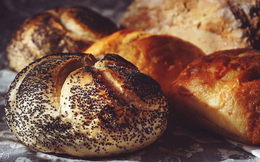 Ein frisches Brötchen mit Mohnsamen, umgeben von weiteren goldbraunen Backwaren auf einem dekorativen Tuch.