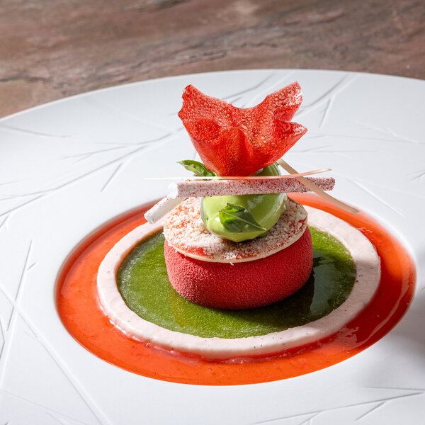 Ein kunstvoll angerichtetes Dessert auf einem weißen Teller, umgeben von leuchtenden Fruchtsaucen und dekorativen Elementen.