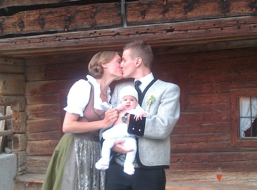 Paar in Tracht küsst sich und hält gemeinsam Baby