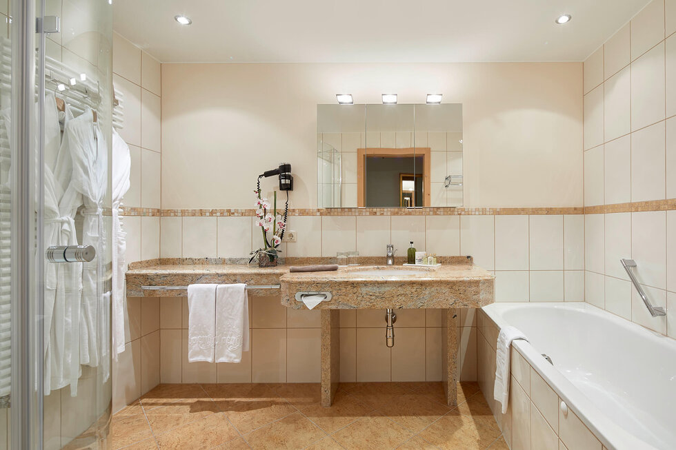 Ein elegantes Badezimmer mit einer Granitoberfläche, einem großen Spiegel und frischen Orchideen auf dem Waschbecken.