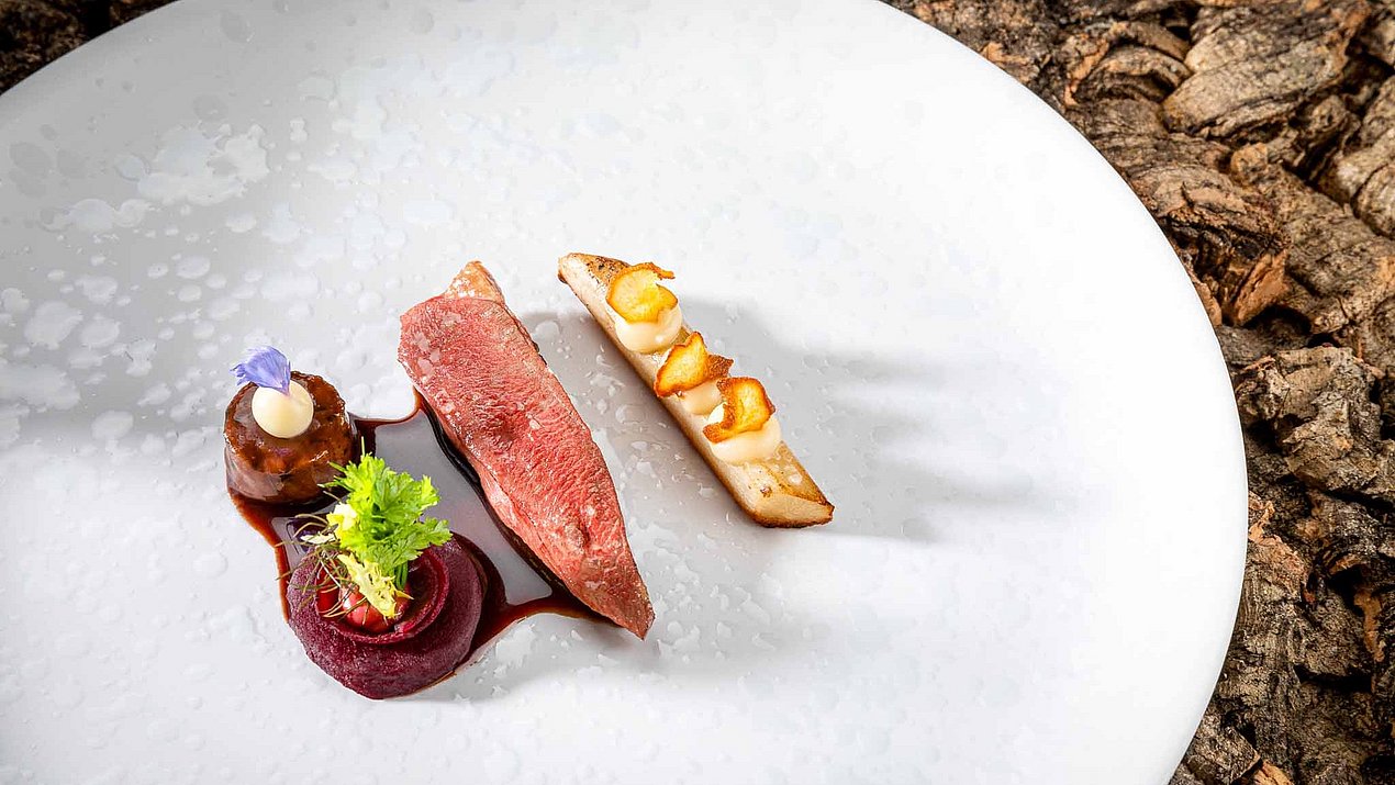 Ein Stückchen Fleisch mit Gemüse liegt auf einem weißen Teller und ist schön dekoriert