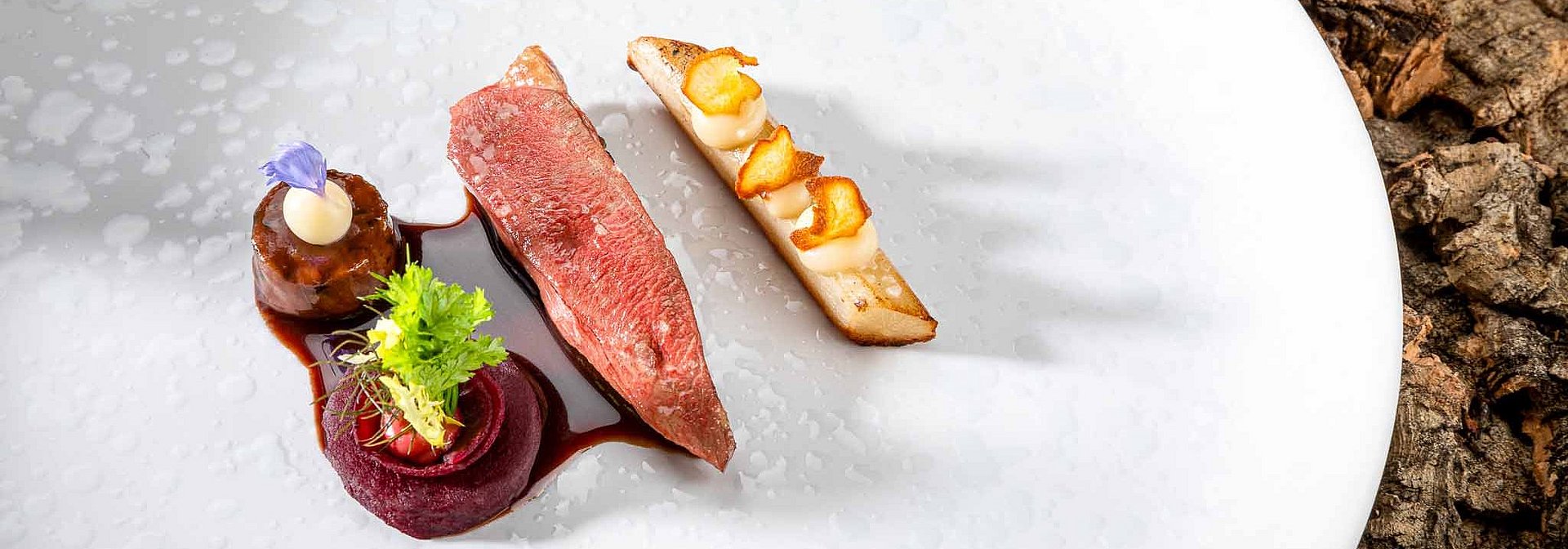 Ein Stückchen Fleisch mit Gemüse liegt auf einem weißen Teller und ist schön dekoriert