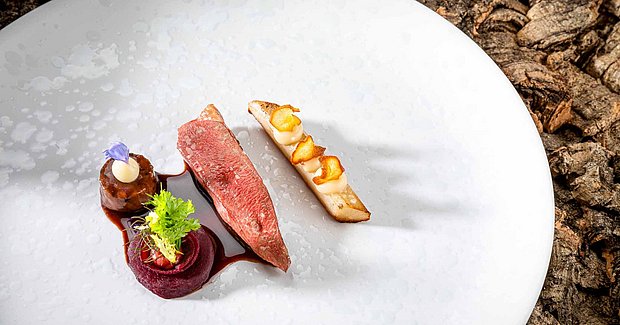 Ein Stückchen Fleisch mit Gemüse liegt auf einem weißen Teller und ist schön dekoriert