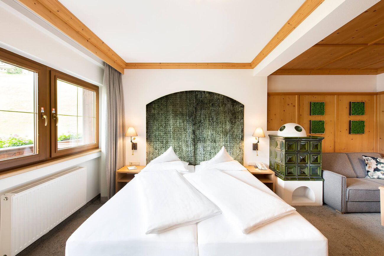 Ein gemütliches Schlafzimmer mit zwei Betten, einem grünen Kopfteil und einem traditionellen Kachelofen in der Ecke.