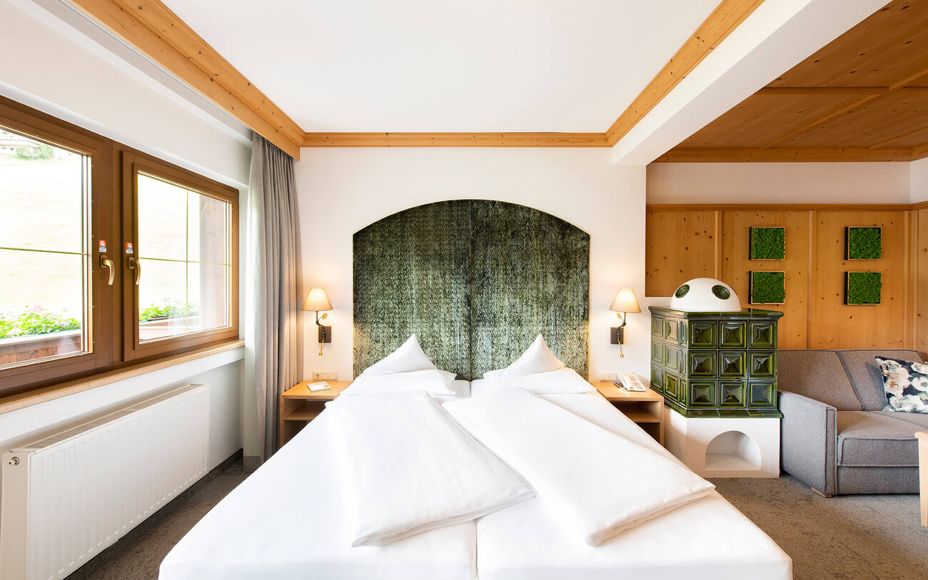 Ein gemütliches Schlafzimmer mit zwei Betten, einem grünen Kopfteil und einem traditionellen Kachelofen in der Ecke.