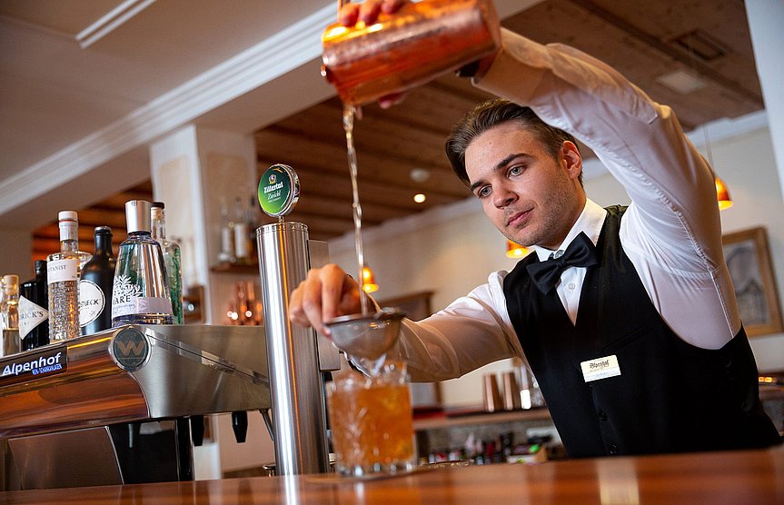 Der Barmann steht hinter der Theke und schenkt einen Cocktail in ein Glas ein.