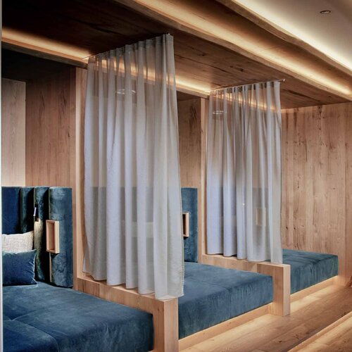 Ein ruhiger Ruheraum mit blauen Polstermöbeln und sanfter Beleuchtung, umgeben von warmem Holz und transparenten Vorhängen.