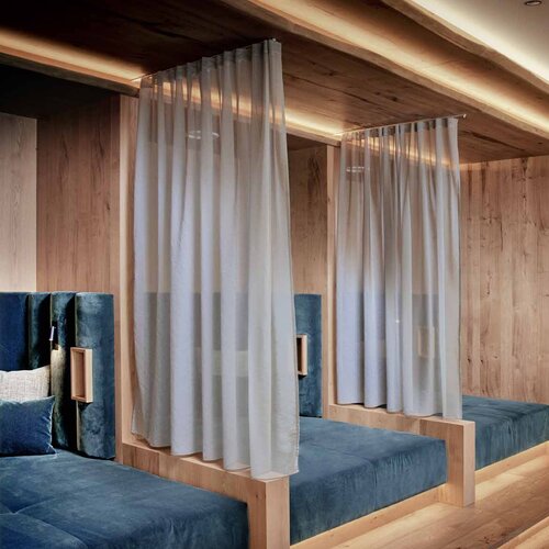 Ein ruhiger Ruheraum mit blauen Polstermöbeln und sanfter Beleuchtung, umgeben von warmem Holz und transparenten Vorhängen.