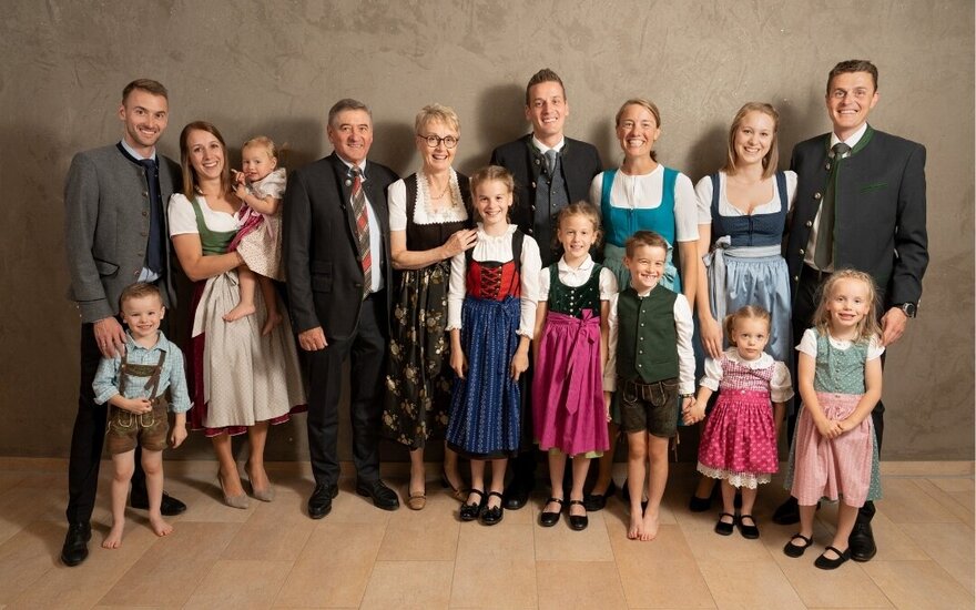 Familienmitglieder in festlicher Tracht stehen eng beieinander, einige halten kleine Kinder, während sie in die Kamera lächeln.