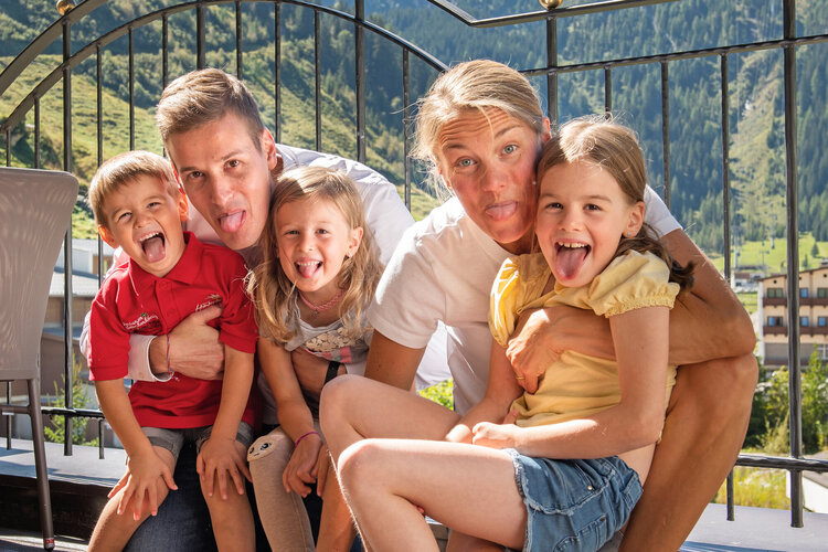 Eine fröhliche Familie posiert vor einer beeindruckenden Berglandschaft, alle zeigen ihre Zungen und lachen herzlich.