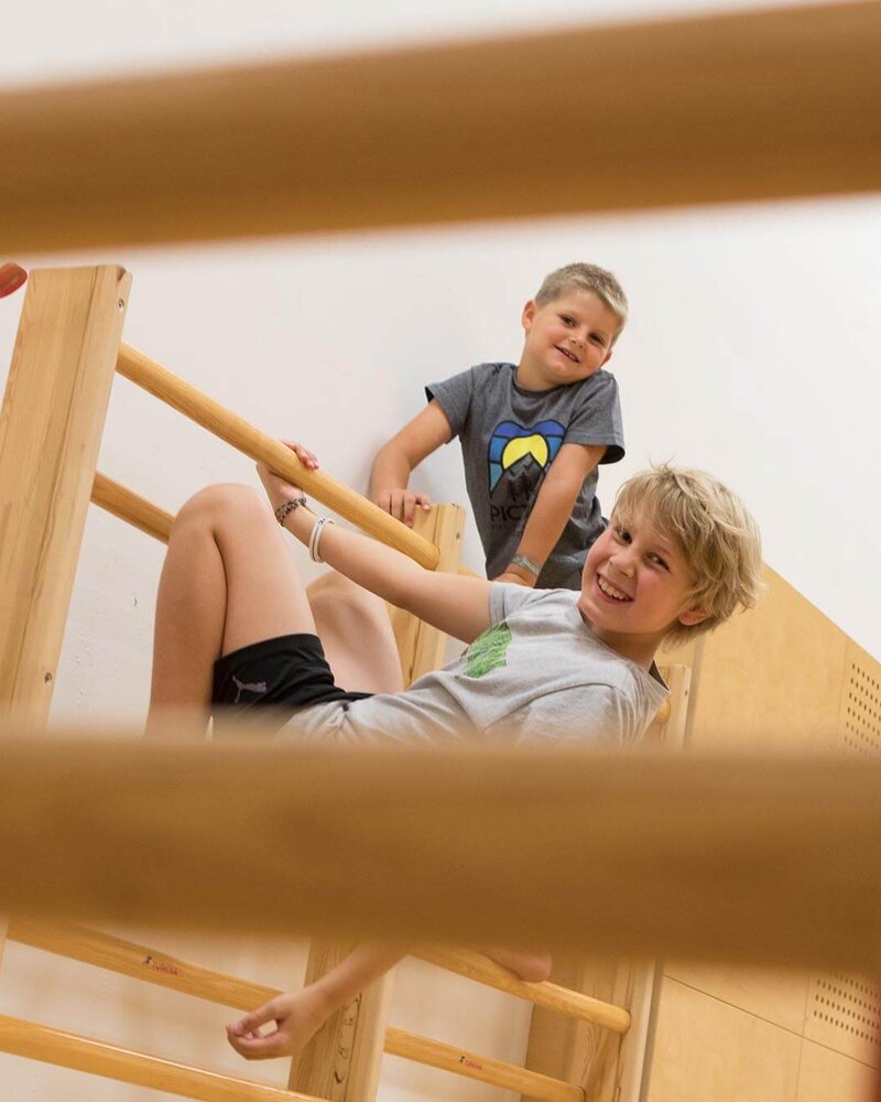 Zwei Kinder spielen fröhlich an einer Sprossenwand in einer Sporthalle, beide lächeln und haben Spaß.