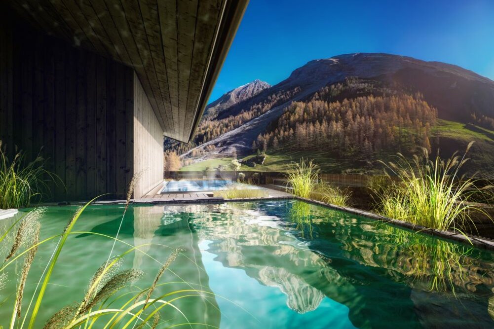 Ein modernes Holzhaus mit einem Pool, umgeben von üppigem Grün und majestätischen Bergen im Hintergrund unter klarem Himmel.