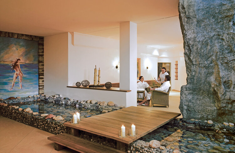 Ein eleganter Spa-Bereich mit einem Holzsteg, umgeben von Wasser und Steinen, schafft eine entspannende Atmosphäre.