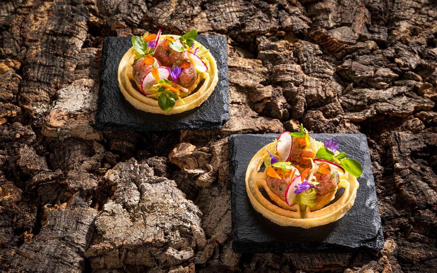 Zwei kunstvoll angerichtete Törtchen auf schwarzen Platten, gefüllt mit buntem Gemüse und essbaren Blüten, auf Holzuntergrund.