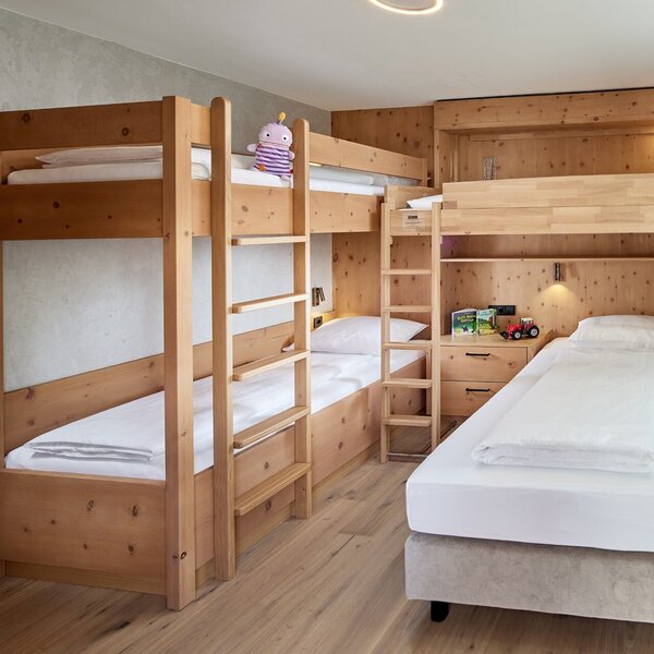 Ein gemütlicher Raum mit zwei Etagenbetten aus Holz und einem Einzelbett, ideal für Kinder oder Familien.