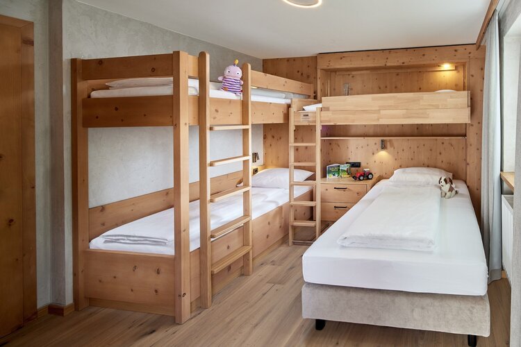 Ein gemütlicher Raum mit zwei Etagenbetten aus Holz und einem Einzelbett, ideal für Kinder oder Familien.