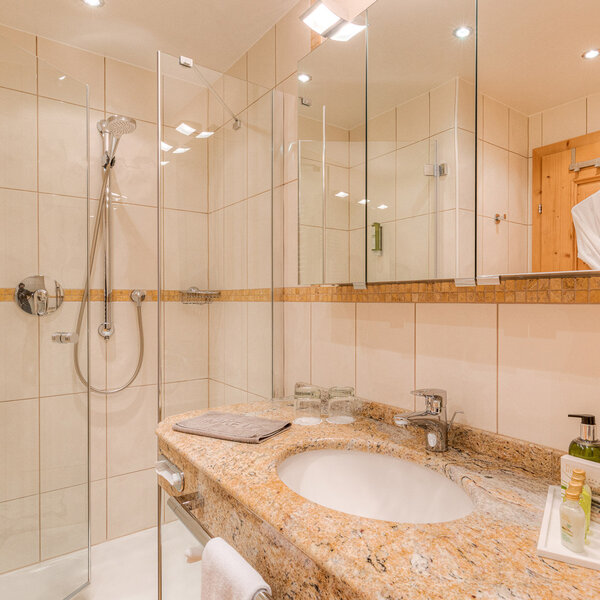 Ein modernes Badezimmer mit einer eleganten Dusche, einem Waschbecken aus Granit und stilvollen Pflegeprodukten auf dem Tisch.