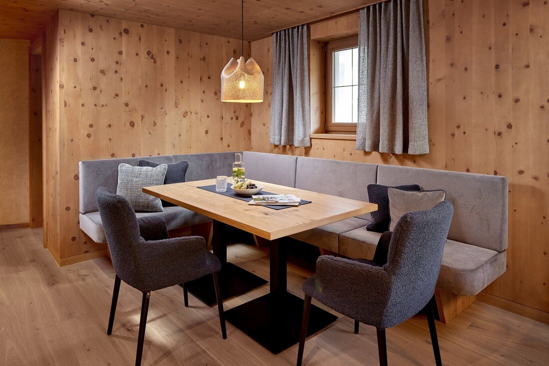 Ein gemütlicher Essbereich mit einer Holzbank und einem Tisch, umgeben von stilvollen Stühlen und warmem Licht.